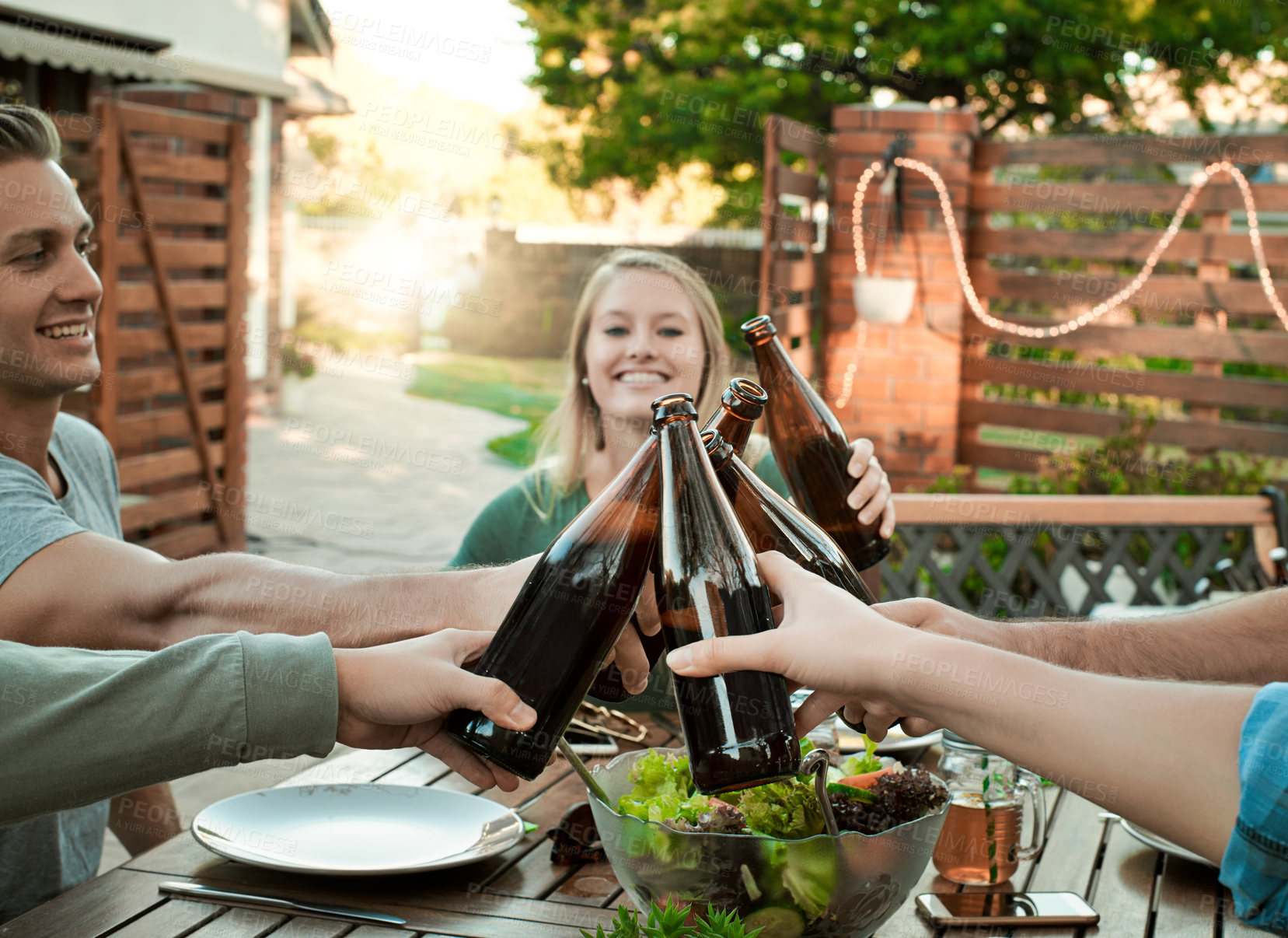 Buy stock photo Dinner, alcohol and friends in garden for cheers, celebration and connection for bonding together. Outdoor, happy people and beer bottle in social gathering for support, united and food for nutrition
