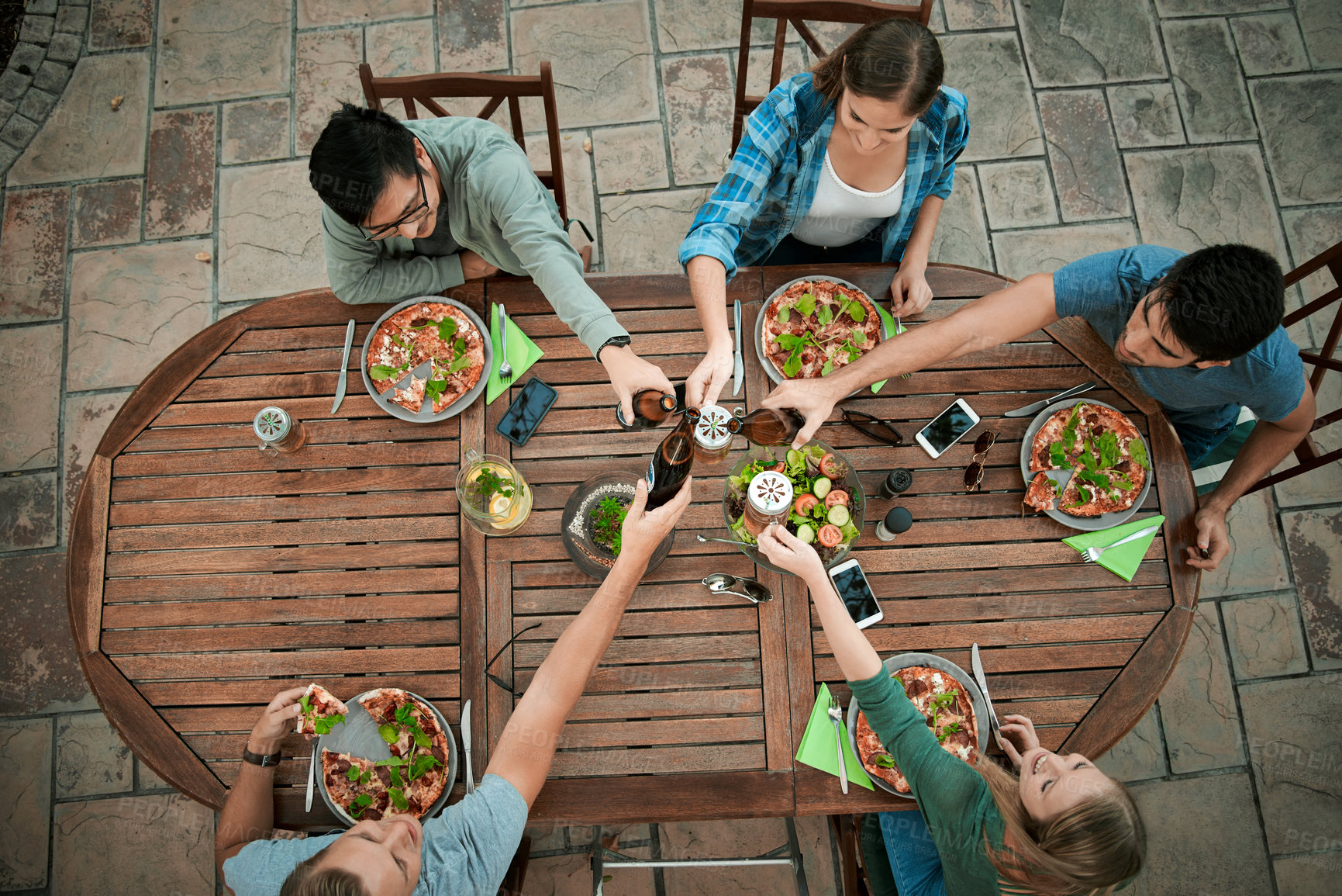 Buy stock photo High angle shot of a group young friends holding drinks and toasting together outside around a table
