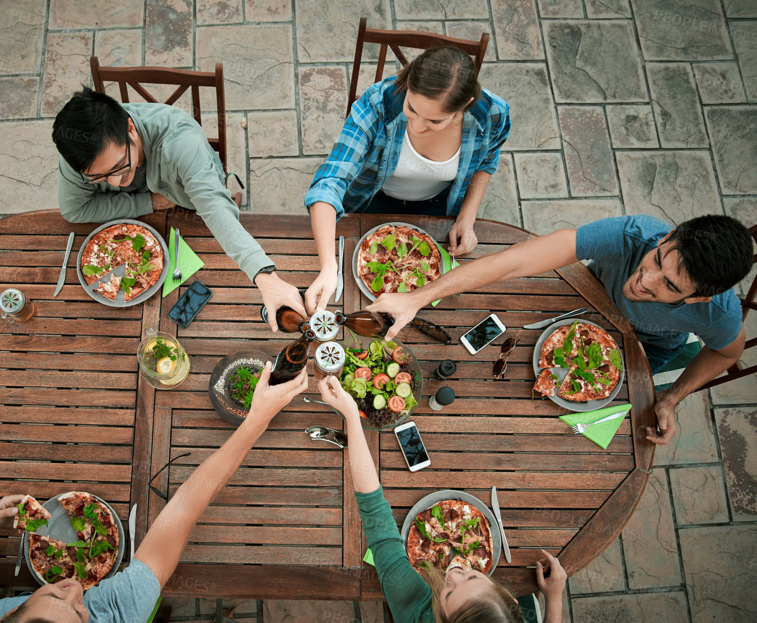 Buy stock photo Dinner, alcohol and people by above for toast, celebration and connection for bonding together. Outdoor, hands and friends with beer bottle in social gathering, cheers and salad as food for nutrition