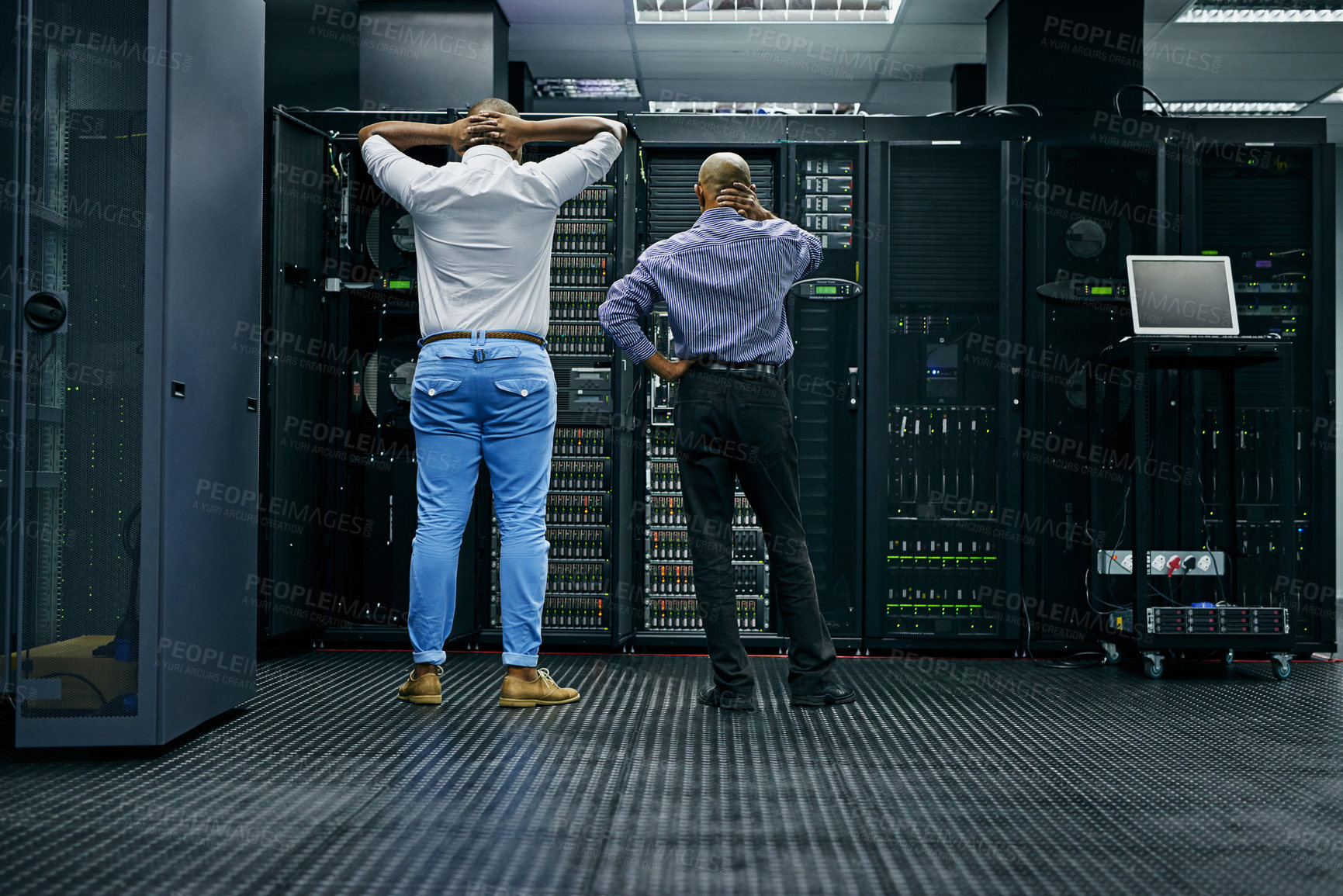Buy stock photo Rearview shot of two IT technicians having difficulty repairing a computer in a data center