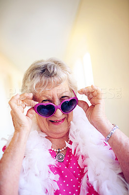 Buy stock photo Shot of a carefree elderly woman putting pink glasses on inside of a building