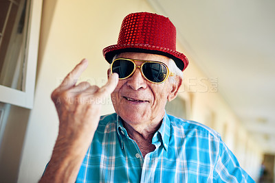 Buy stock photo Shot of a carefree elderly man wearing sunglasses and a hat while showing a hand gesture to the camera inside a building