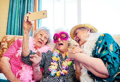 Buy stock photo Shot of a group carefree elderly people wearing funky costumes and getting close for a selfie inside of a building