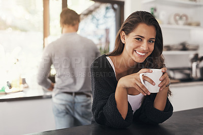 Buy stock photo Shot of a young woman having coffee in the kitchen with her boyfriend standing in the background
