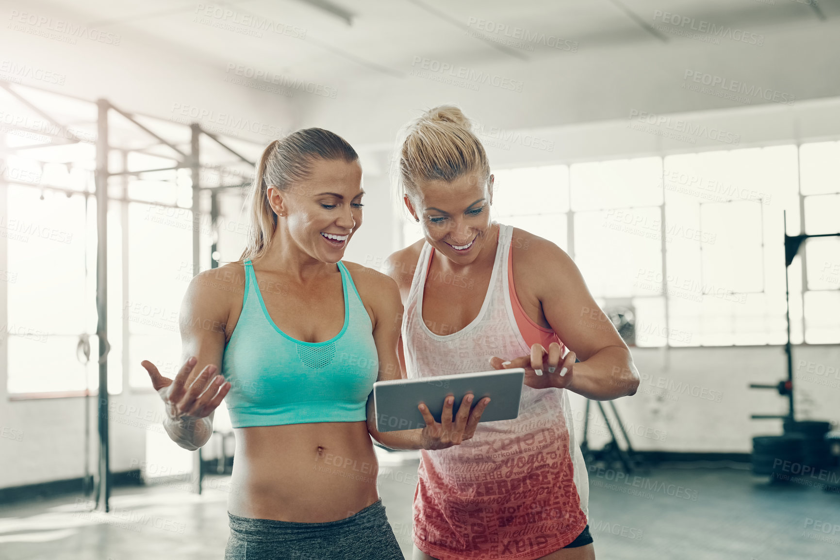 Buy stock photo Shot of two young women using a digital tablet at the gym