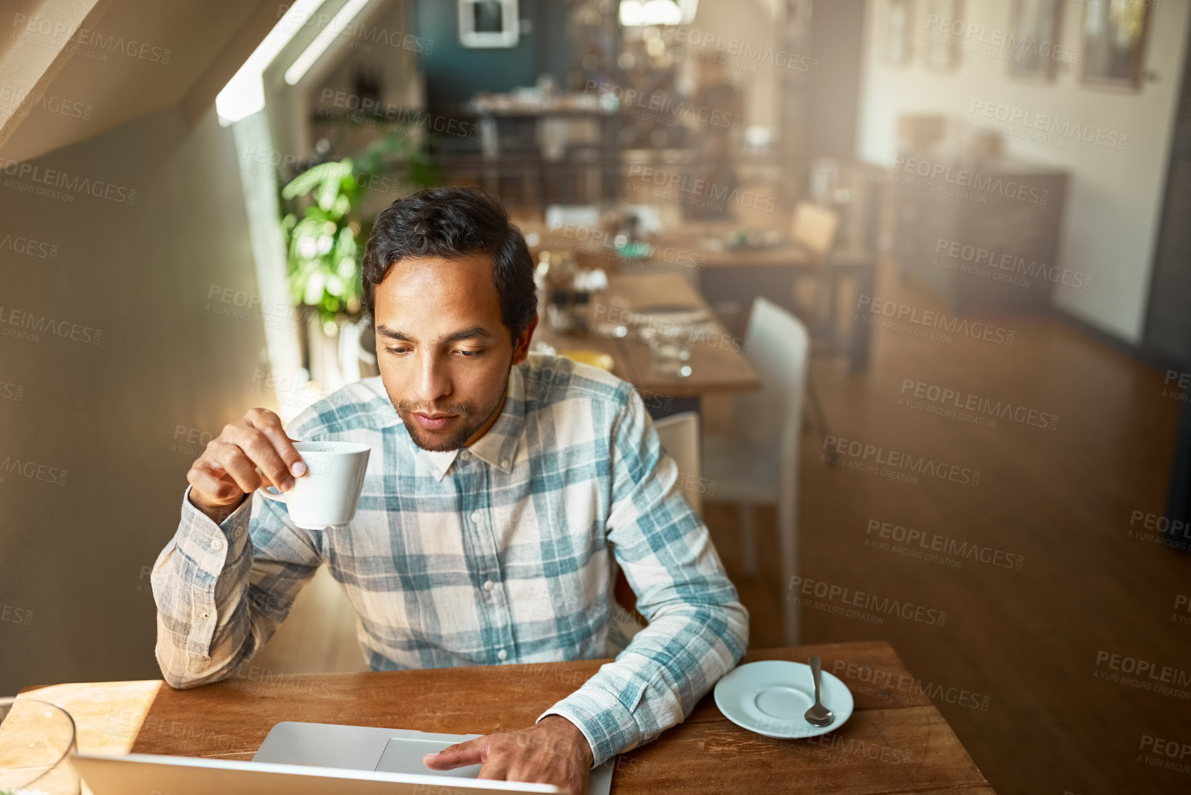 Buy stock photo Shot of a young entrepreneur using his laptop in a coffee shop