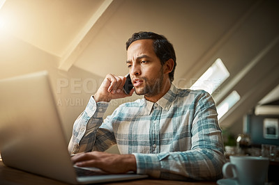 Buy stock photo Shot of a young man talking on his phone while using his laptop