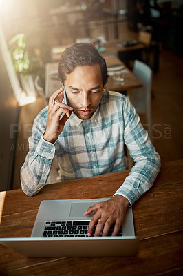 Buy stock photo Shot of a young man talking on his phone while using his laptop