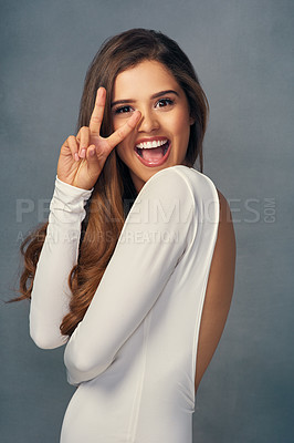 Buy stock photo Studio portrait of an attractive young woman showing a peace sign against a grey background