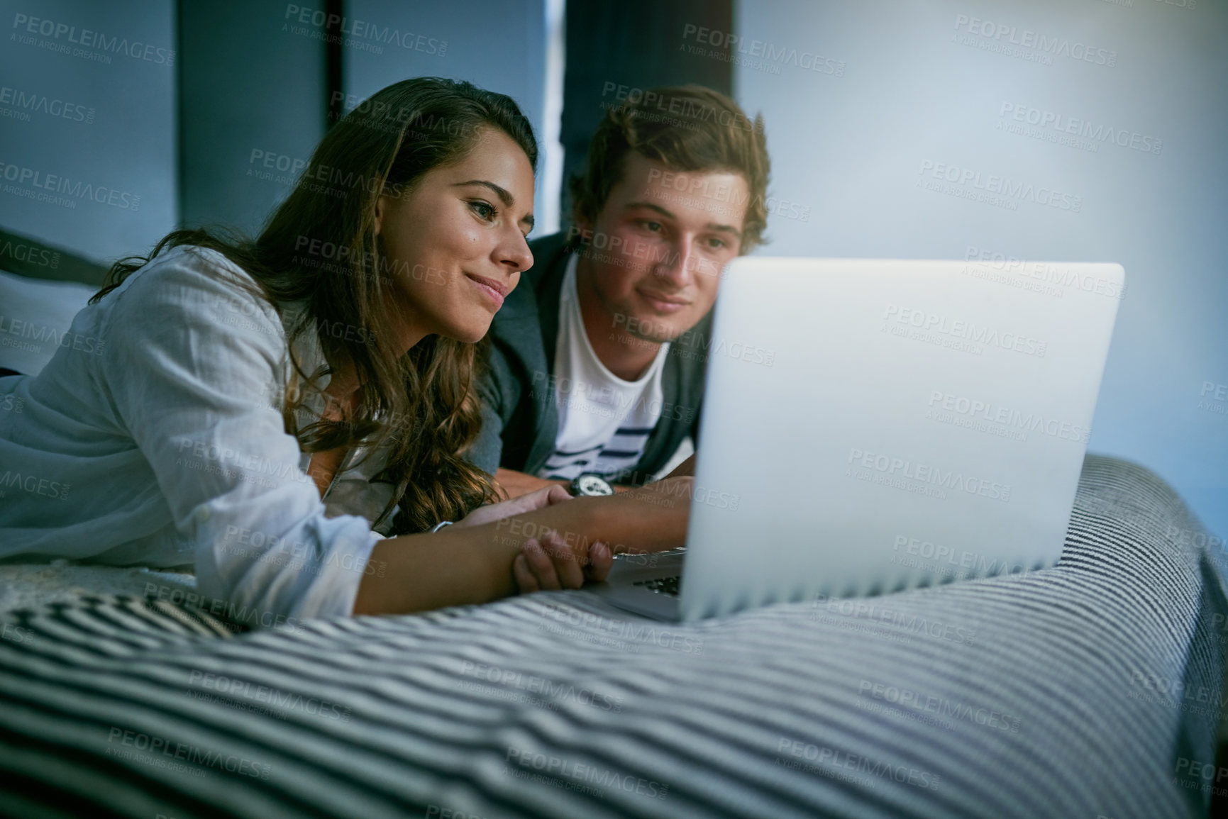 Buy stock photo Shot of a young couple using their laptop together while lying on bed