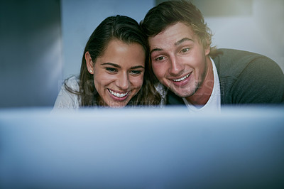 Buy stock photo Shot of a young couple using their laptop together while lying on bed