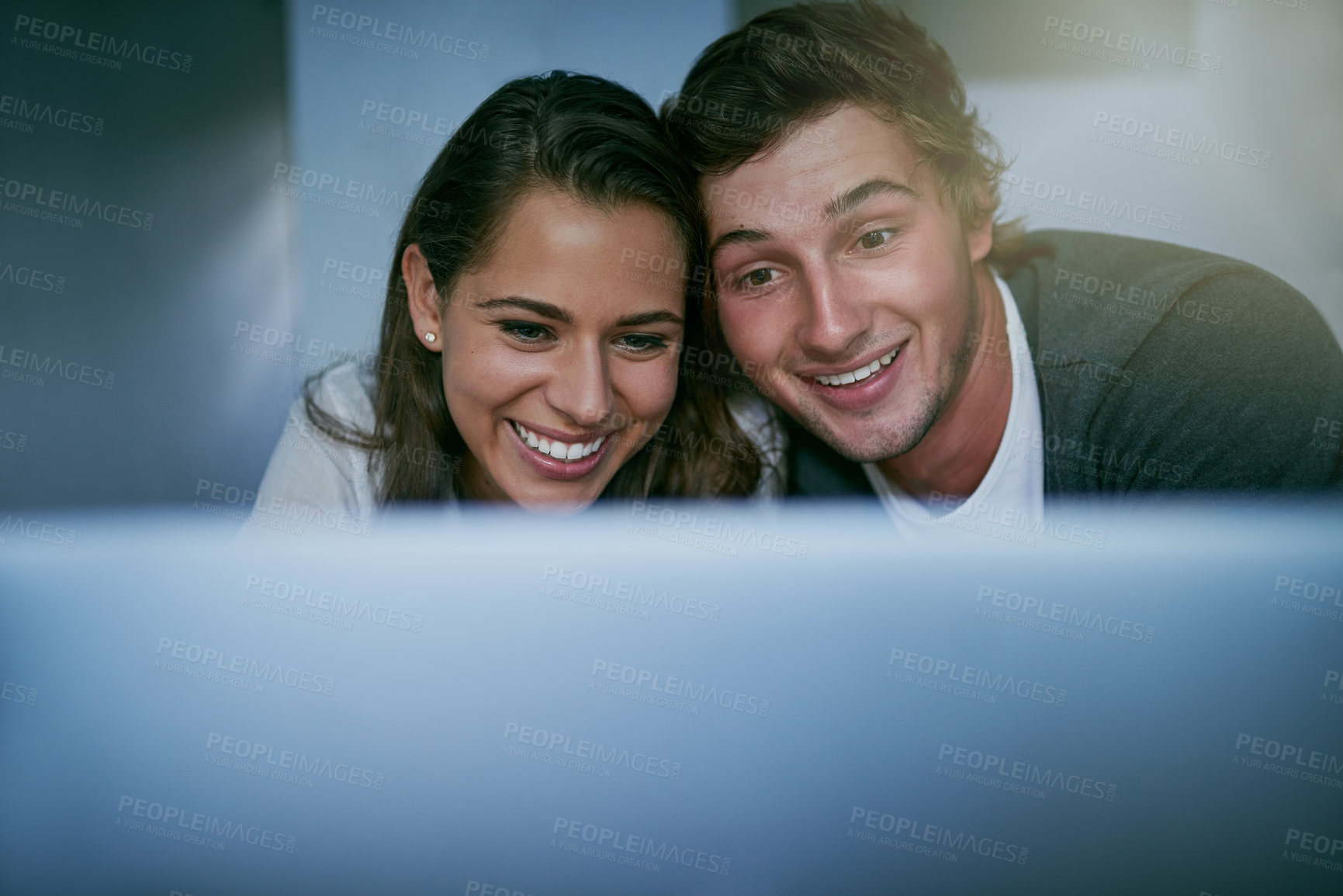 Buy stock photo Shot of a young couple using their laptop together while lying on bed