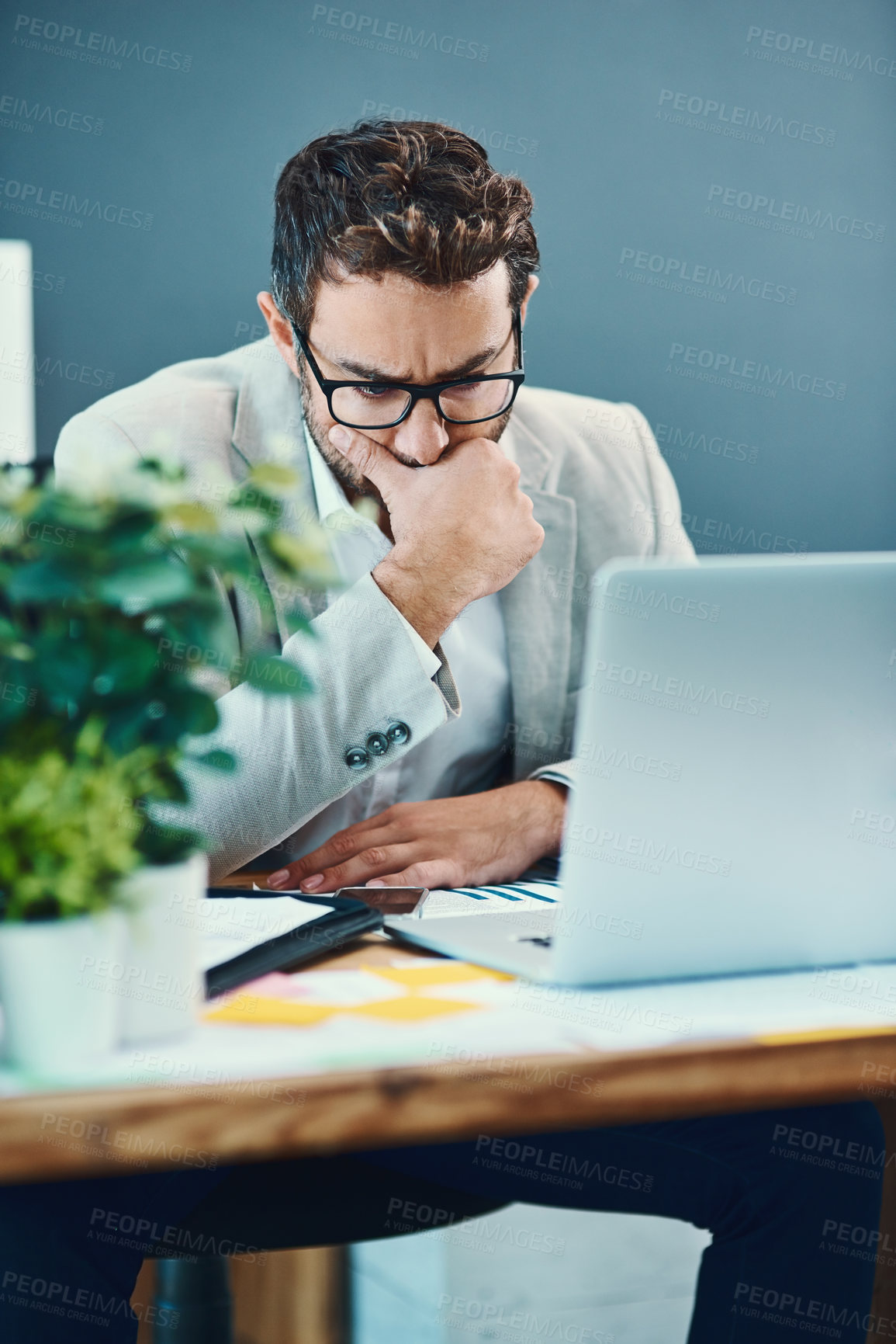 Buy stock photo Shot of a young businessman looking stressed out while working on a laptop in an office