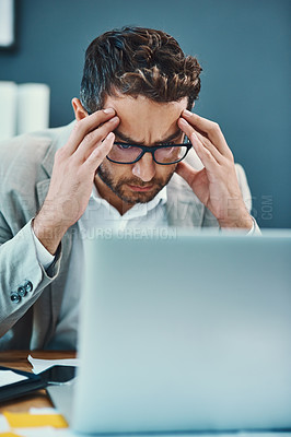 Buy stock photo Shot of a young businessman looking stressed out while working on a laptop in an office
