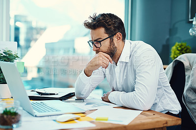 Buy stock photo Shot of a young businessman looking serious while working on a laptop in an office