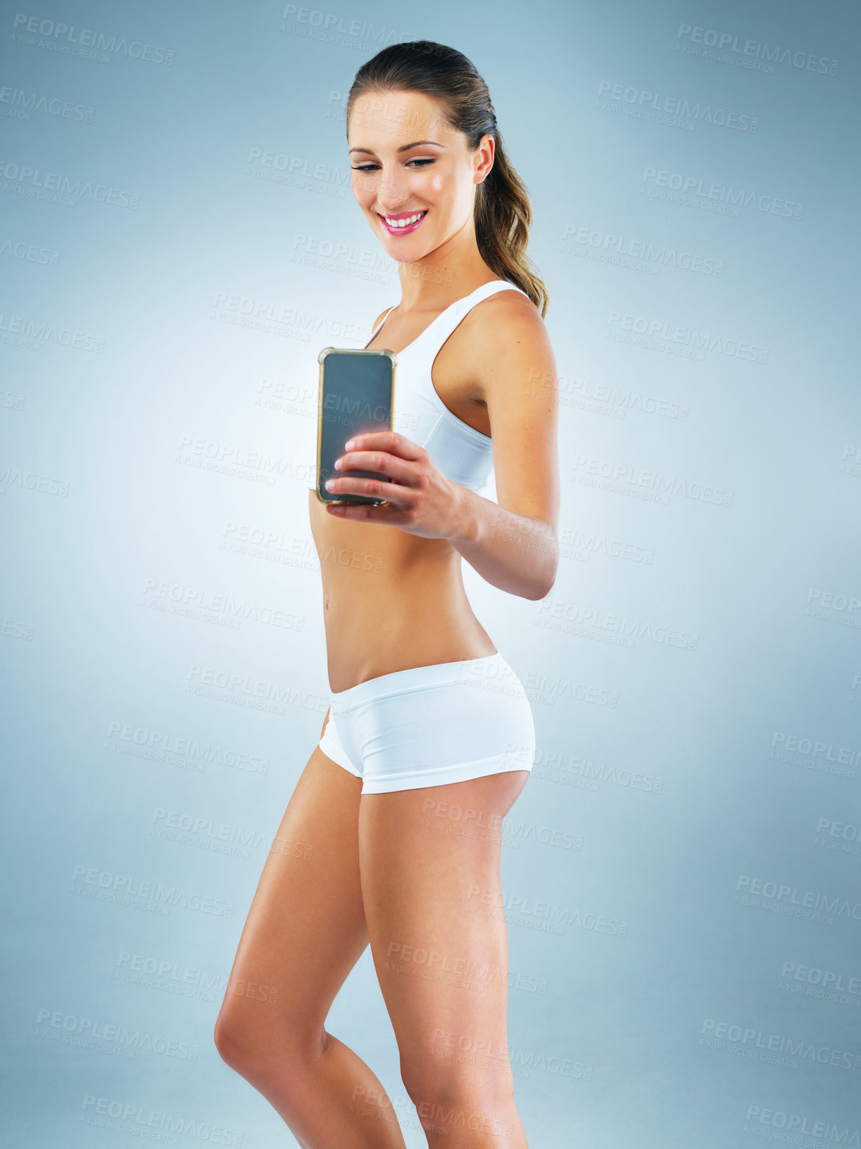 Buy stock photo Cellphone, fitness and woman in studio with weightloss progress for nutrition, wellness and body goals. Diet, phone and slim female person with photography picture for health by gray background.