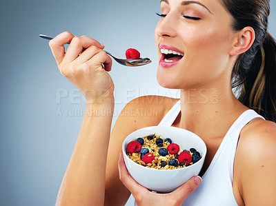 Buy stock photo Happy woman, eating and bowl with fruit for diet or nutrition on a blue studio background. Young female person or model with smile or spoon for natural organic muesli, healthy wheat or vitamin fiber