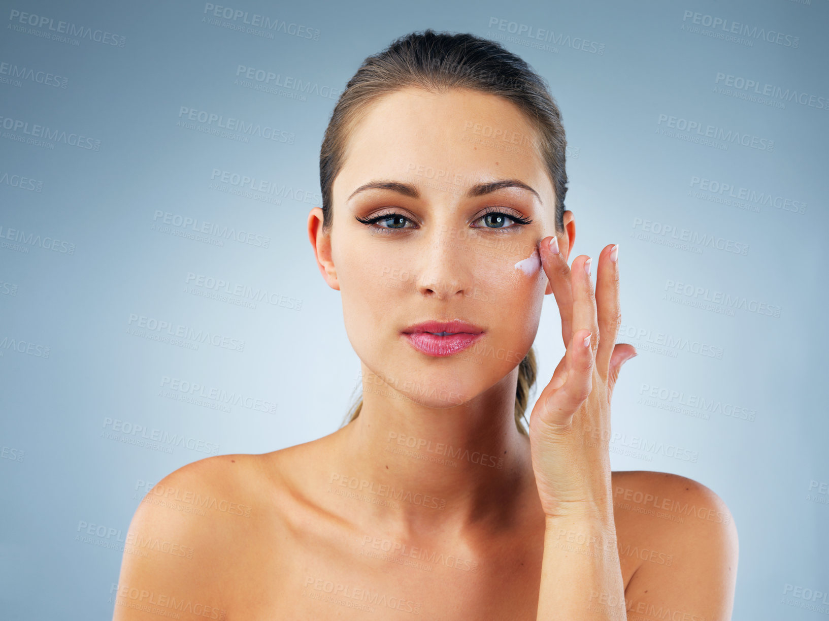 Buy stock photo Woman, face cream and studio with hand, beauty or wellness with moisturizer in portrait by blue background. Person, girl and model with creme, product and facial cosmetics for skincare transformation