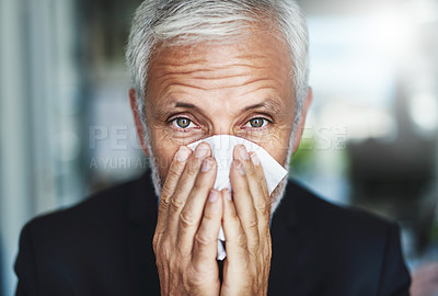 Buy stock photo Shot of a frustrated businessman using a tissue to sneeze in while being seated in the office