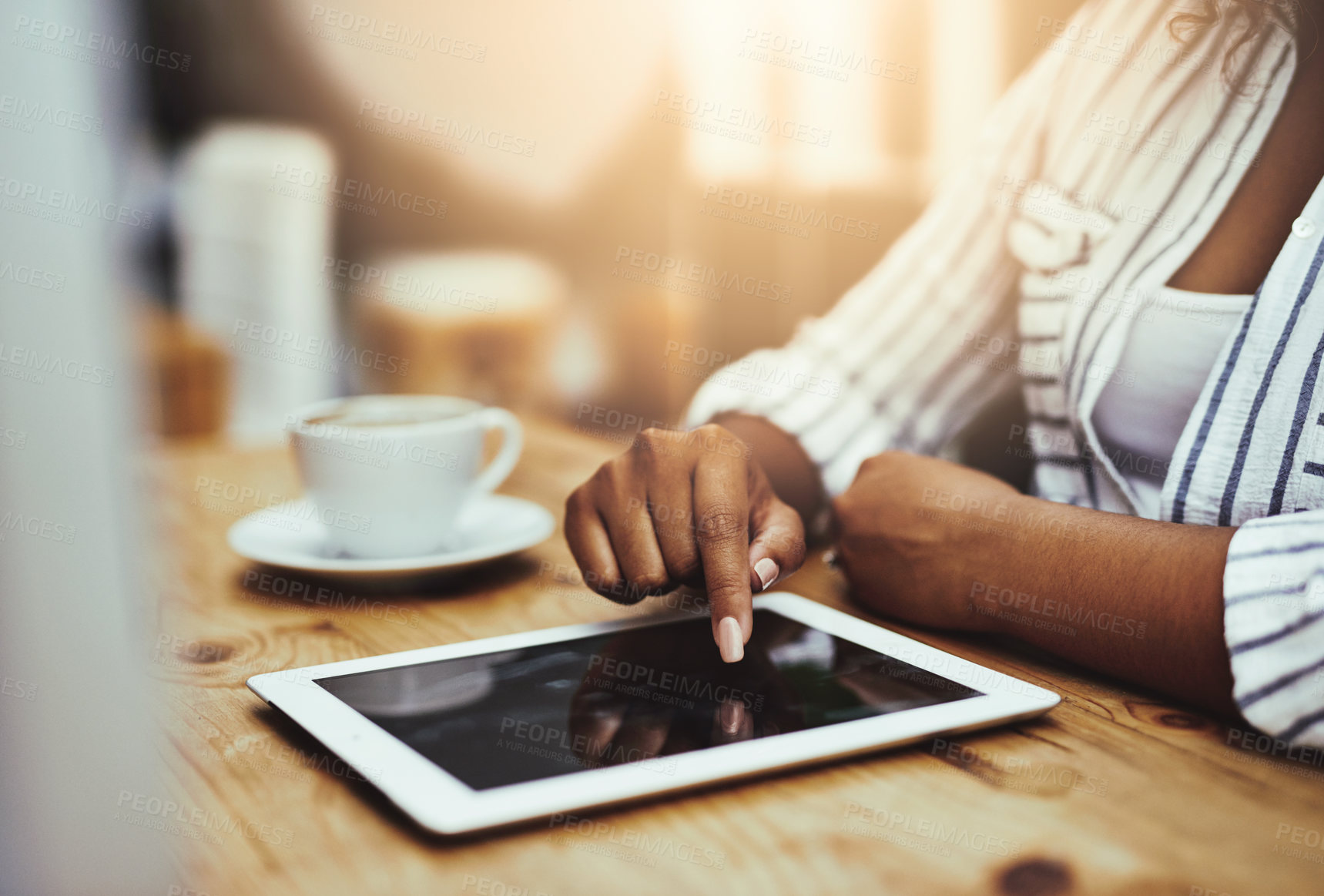 Buy stock photo African woman working on a tablet, sitting in a cafe with coffee alone. Businesswoman using technology to do her job at her desk in the office. Lady casually scrolling the internet in a restaurant.