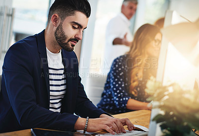 Buy stock photo Cropped shot of a young designer working at his desk with his colleagues in the background