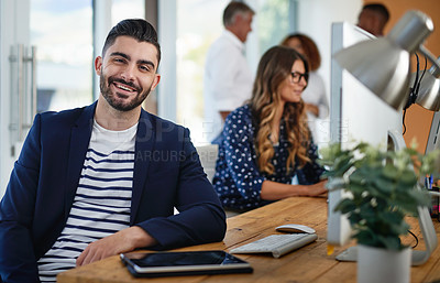 Buy stock photo Portrait of a young designer sitting at his desk with his colleagues in the background