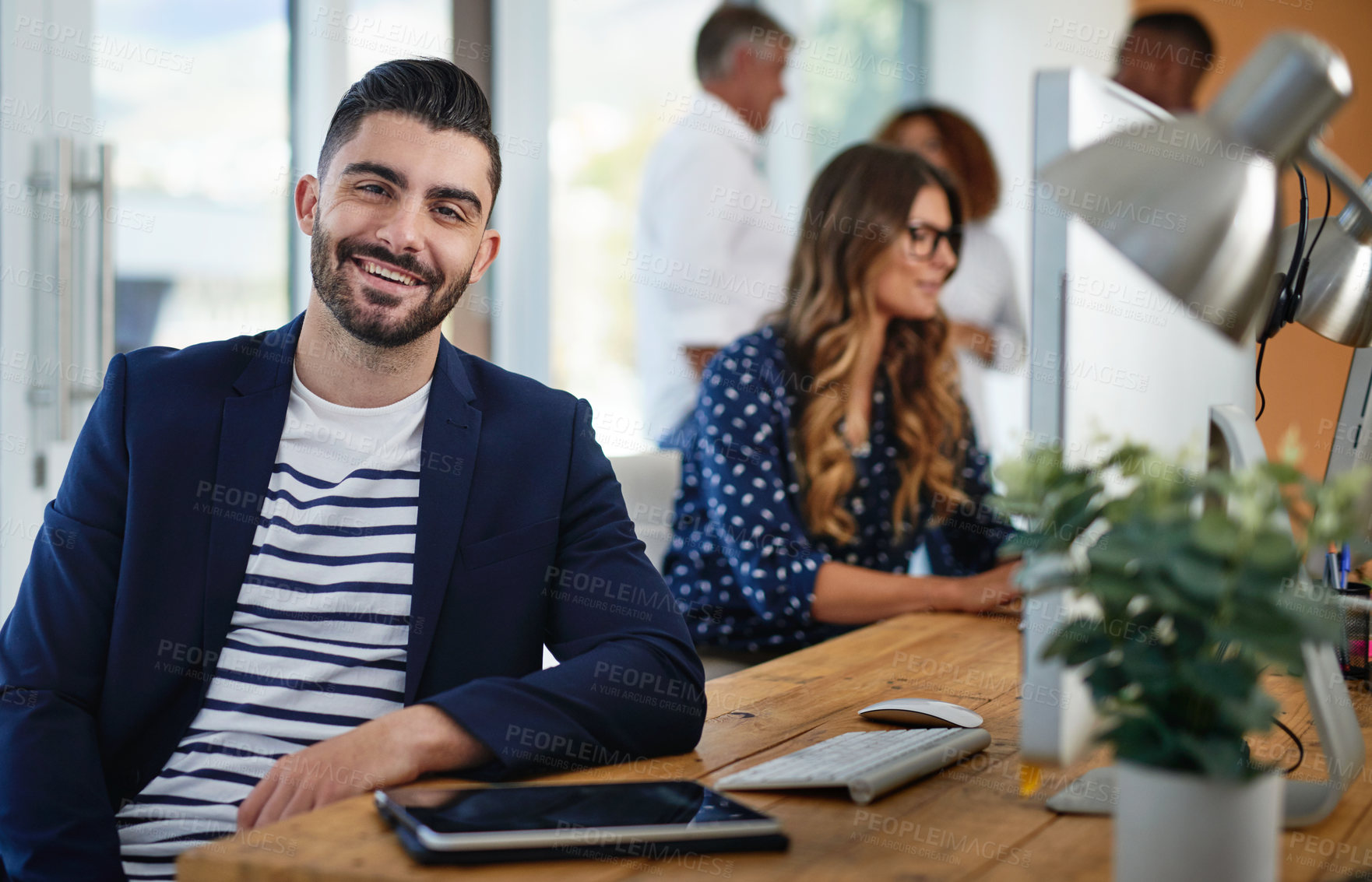 Buy stock photo Creative, coworking and portrait of man at desk with smile, confidence and team at digital agency. Computer, tablet and designer in office with happy face, business people and online connectivity.