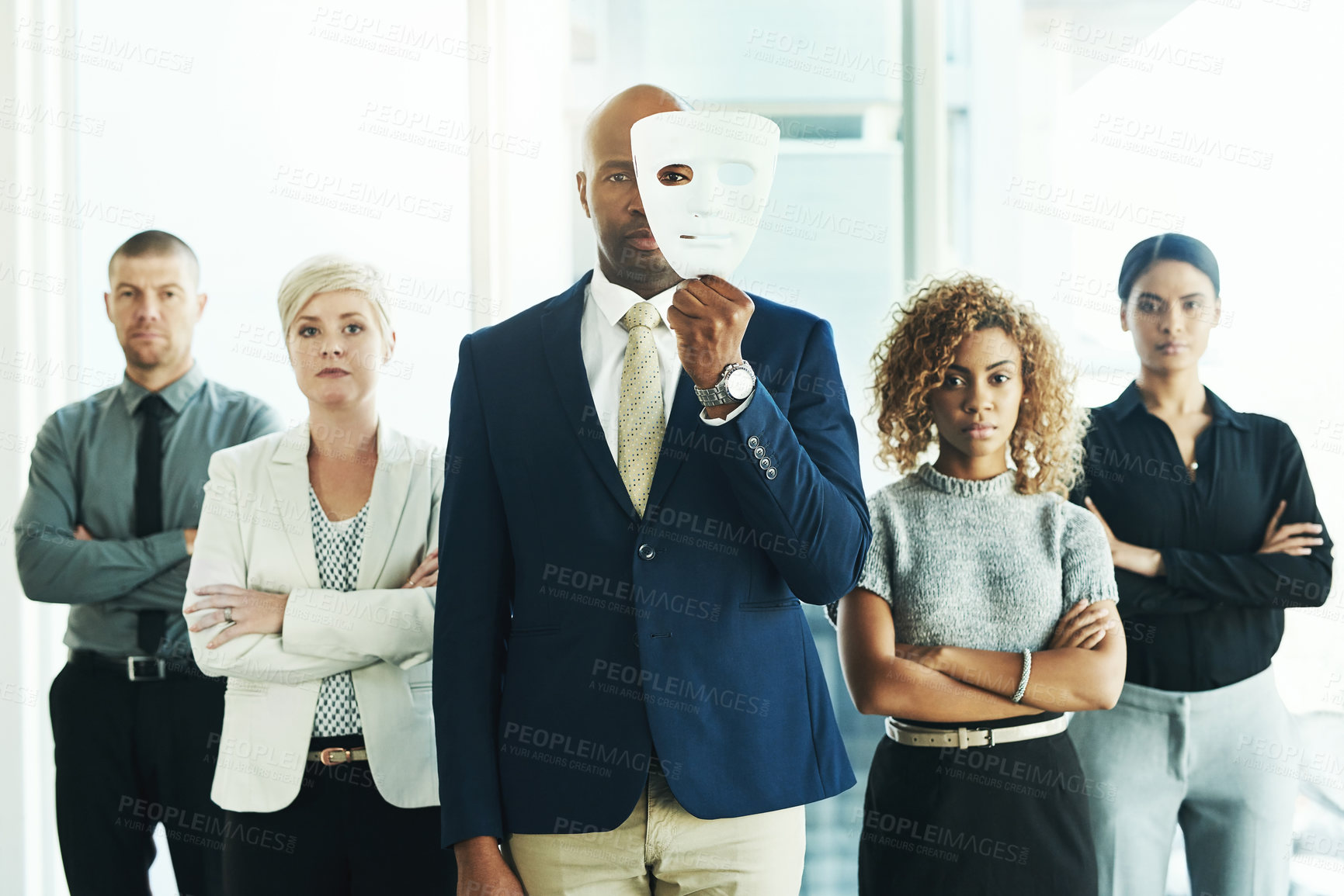 Buy stock photo Portrait of a businessman holding a mask in front of his face with his colleagues standing alongside him in an office