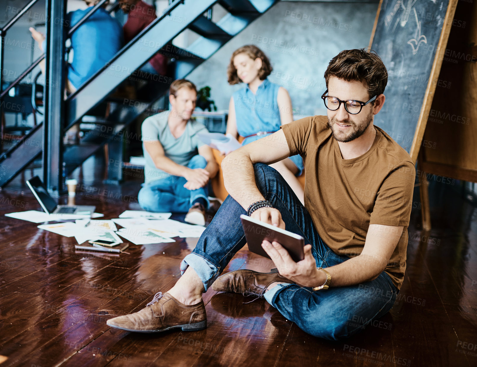 Buy stock photo Shot of a young designer working on a digital tablet with his colleagues in the background