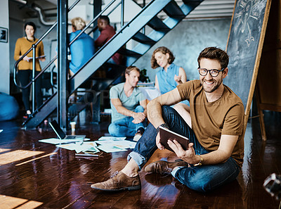 Buy stock photo Portrait of a young designer working on a digital tablet with his colleagues in the background