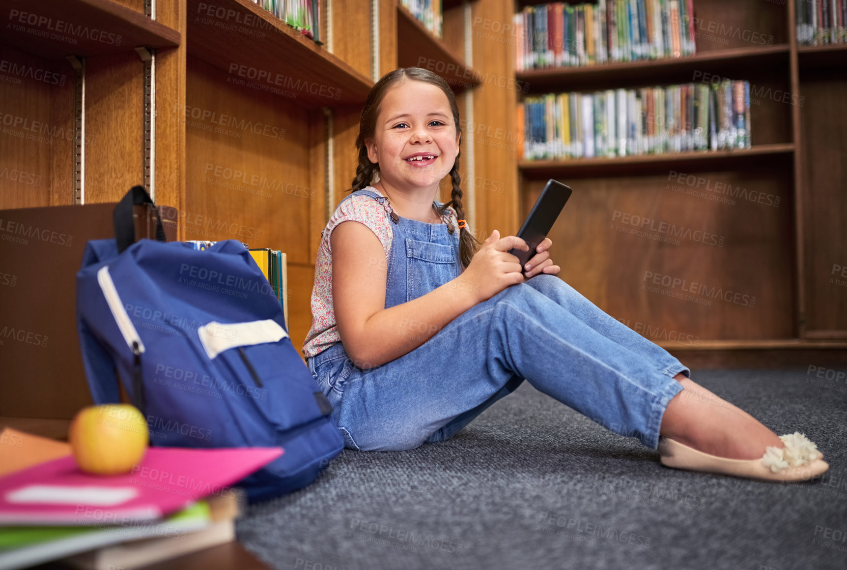 Buy stock photo Library, portrait and happy child learning on tablet at school for knowledge in kindergarten. Bookshelf, student and girl studying on tech for english test, course and educational game on floor in Uk