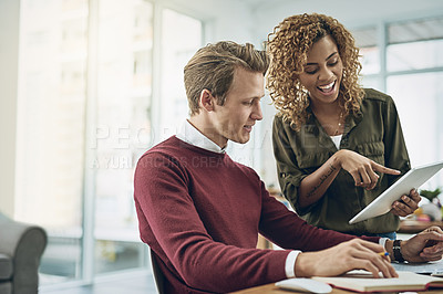 Buy stock photo Shot of two young colleagues using a digital tablet together in a modern office