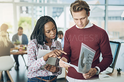 Buy stock photo Shot of two young colleagues discussing paperwork together in a modern office