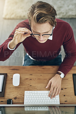 Buy stock photo High angle shot of a young man using a computer at his desk in a modern office