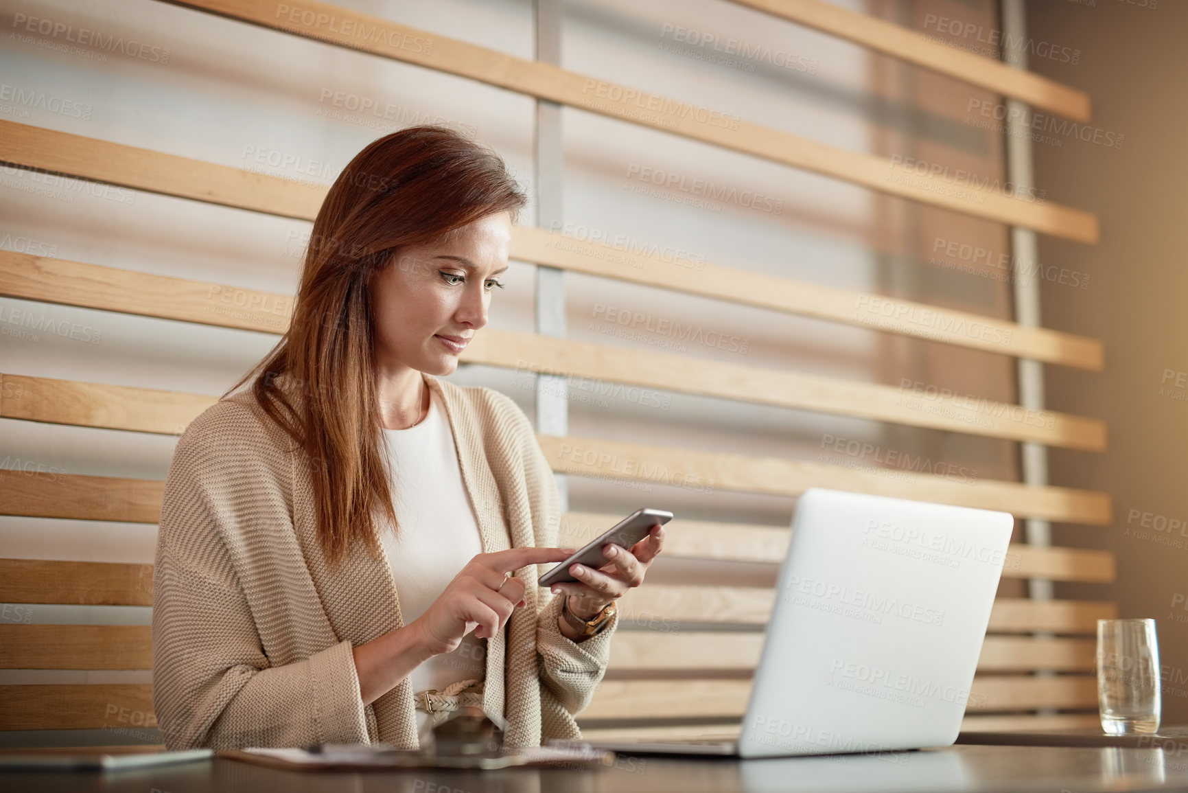 Buy stock photo Shot of a young woman working her cellphone and laptop in a cafe