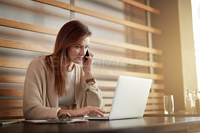 Buy stock photo Shot of a young woman talking on a cellphone while working on her laptop in a cafe