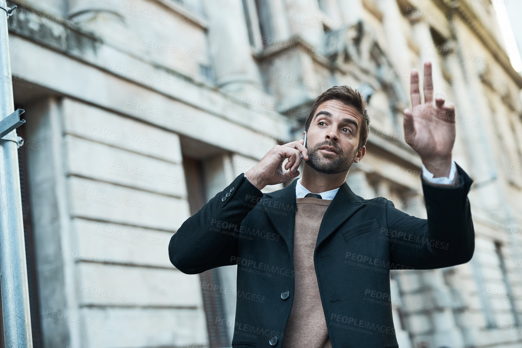 Buy stock photo Cropped shot of a handsome businessman hailing a cab while making a phonecall