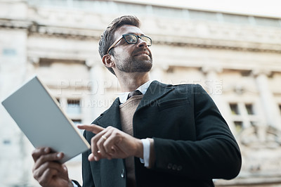 Buy stock photo Low angle shot of a handsome businessman using his tablet while about town