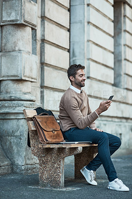 Buy stock photo Full length shot of a handsome businessman using his cellphone while sitting on a bench in town
