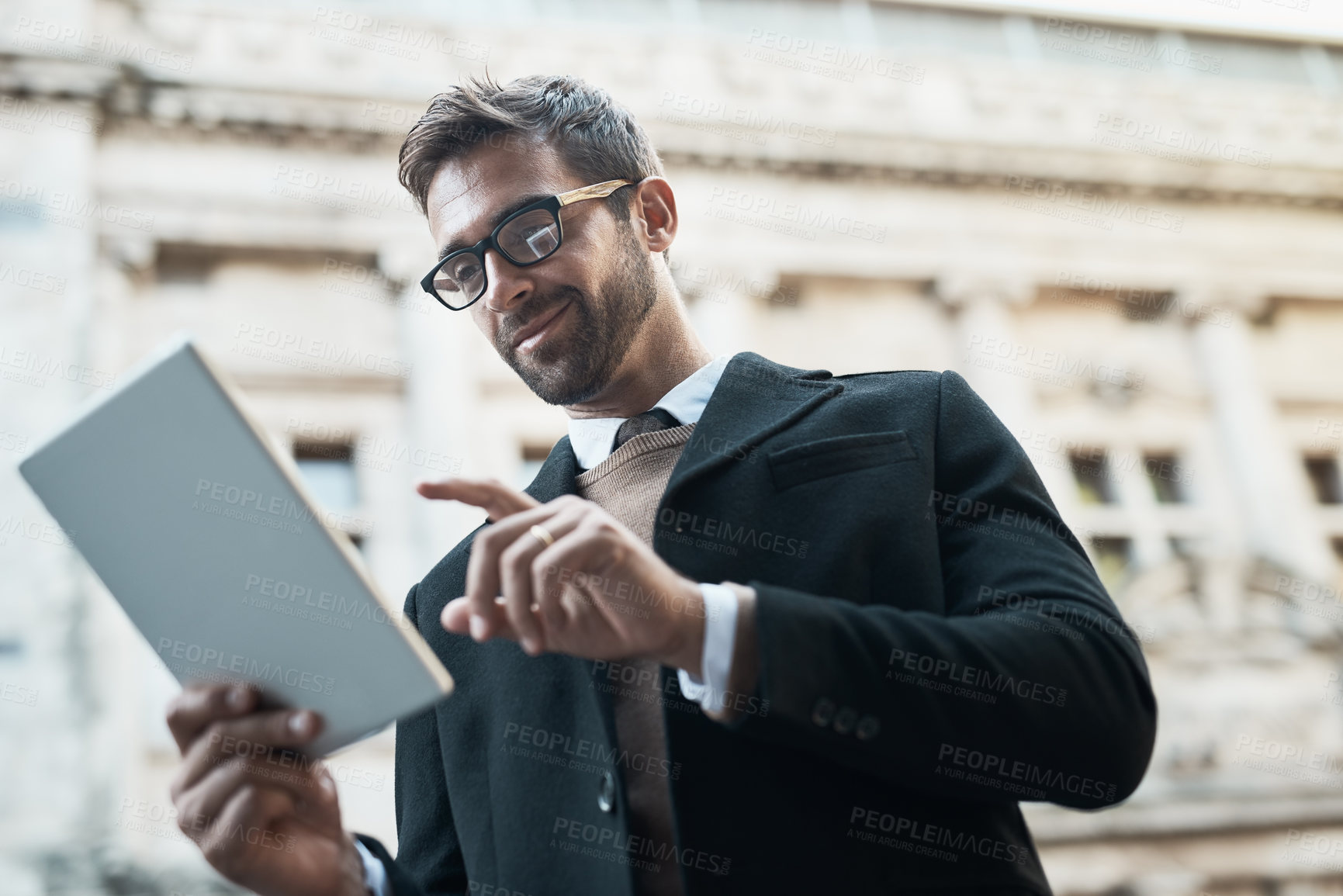 Buy stock photo Low angle shot of a handsome businessman using his tablet while about town