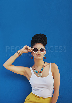Buy stock photo Studio shot of an attractive young woman wearing funky sunglasses and pouting against a blue background