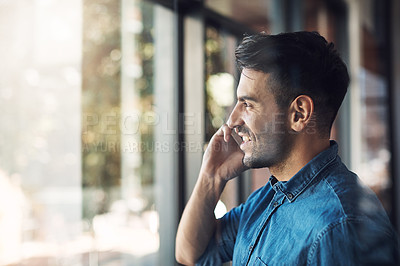 Buy stock photo Smiling casual man on a phone call looking out a window indoors. Happy modern male with a smile standing alone talking on his mobile. Attractive guy inside holding his smartphone feeling confident