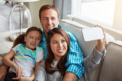 Buy stock photo Interracial parents, child and selfie on sofa for smile, hug and relax with care, mobile app or memory in home. Father, mother and daughter for embrace, social media or love on couch in family house