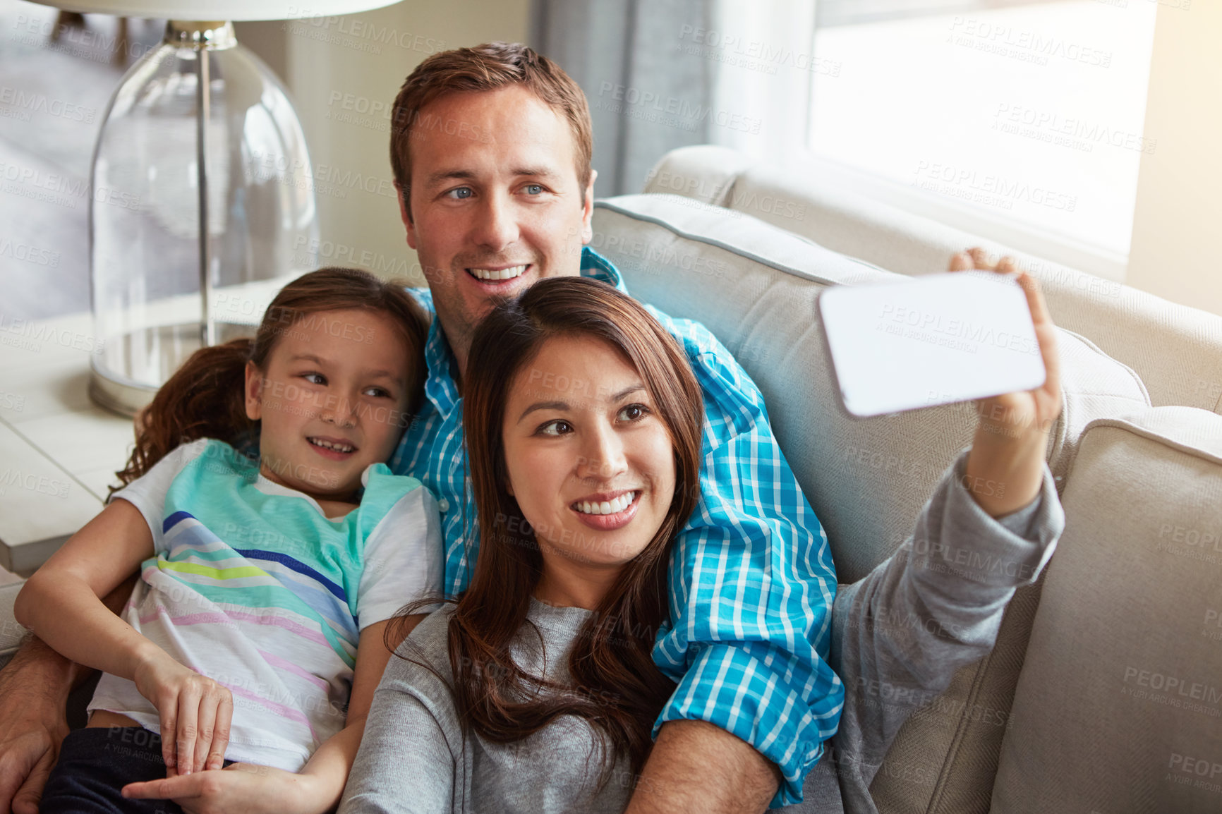 Buy stock photo Interracial parents, child and selfie on sofa for smile, hug and relax with care, mobile app or memory in home. Father, mother and daughter for embrace, social media or love on couch in family house