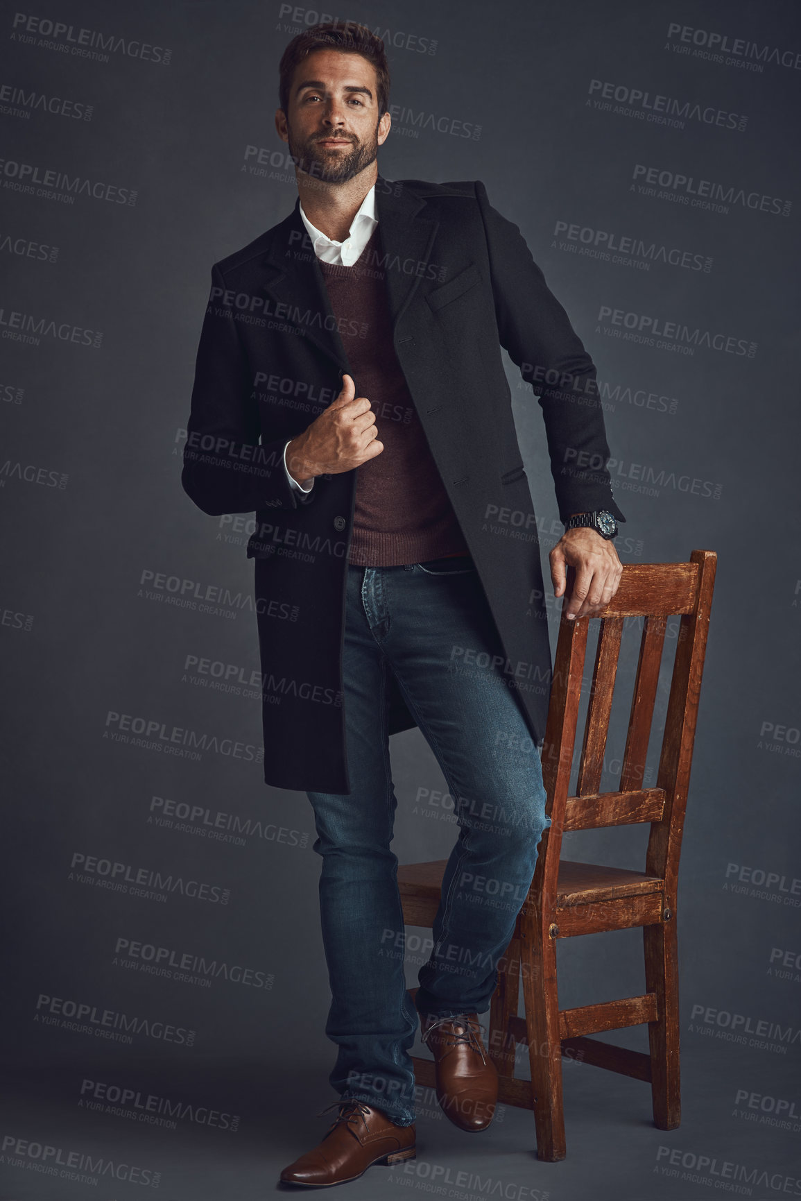 Buy stock photo Studio portrait of a stylishly dressed young man standing next to a chair against a gray background