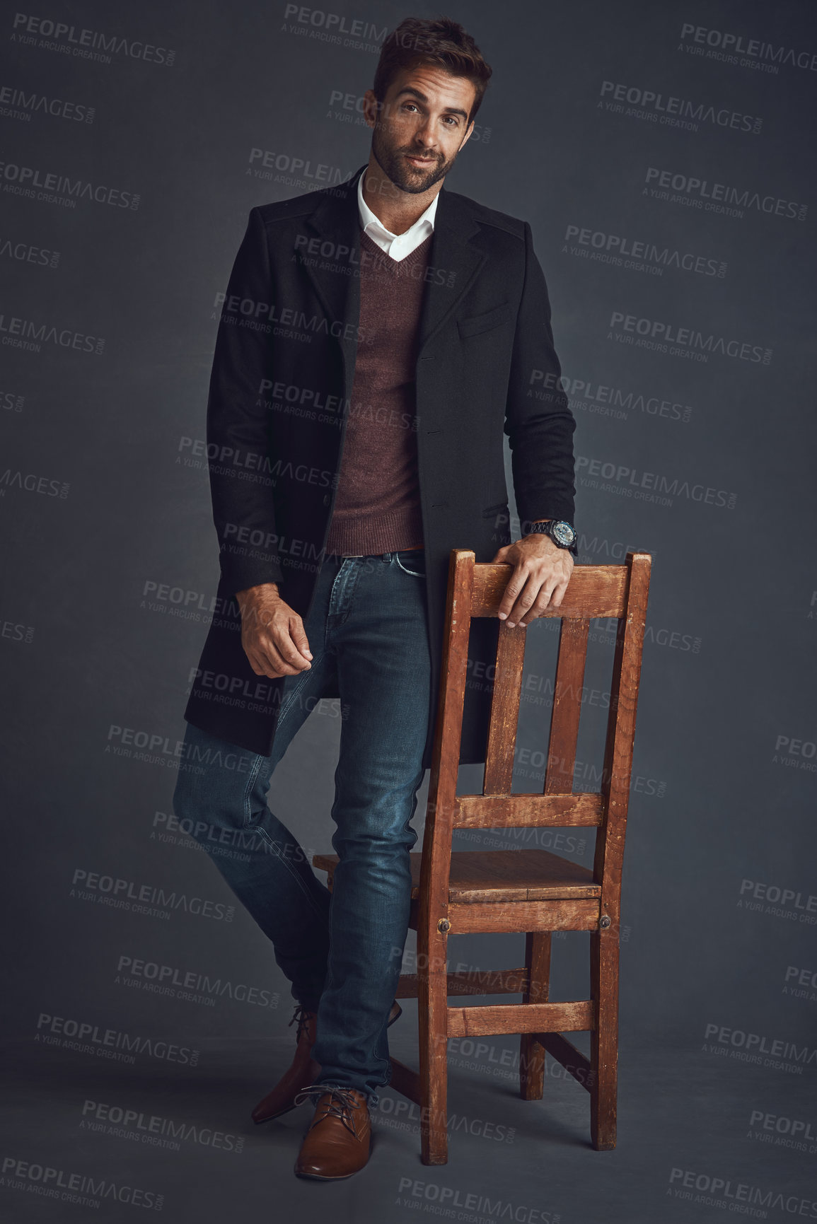 Buy stock photo Studio portrait of a stylishly dressed young man standing next to a chair against a gray background