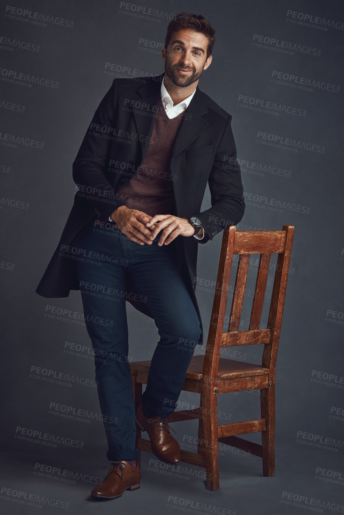 Buy stock photo Studio portrait of a stylishly dressed young man standing next to a chair against a gray background