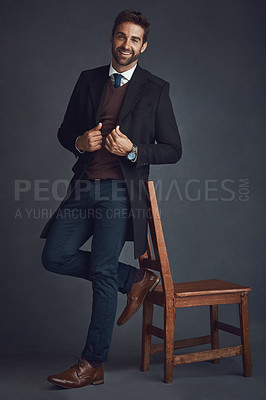 Buy stock photo Studio portrait of a stylishly dressed young man standing next to a chair against a gray background