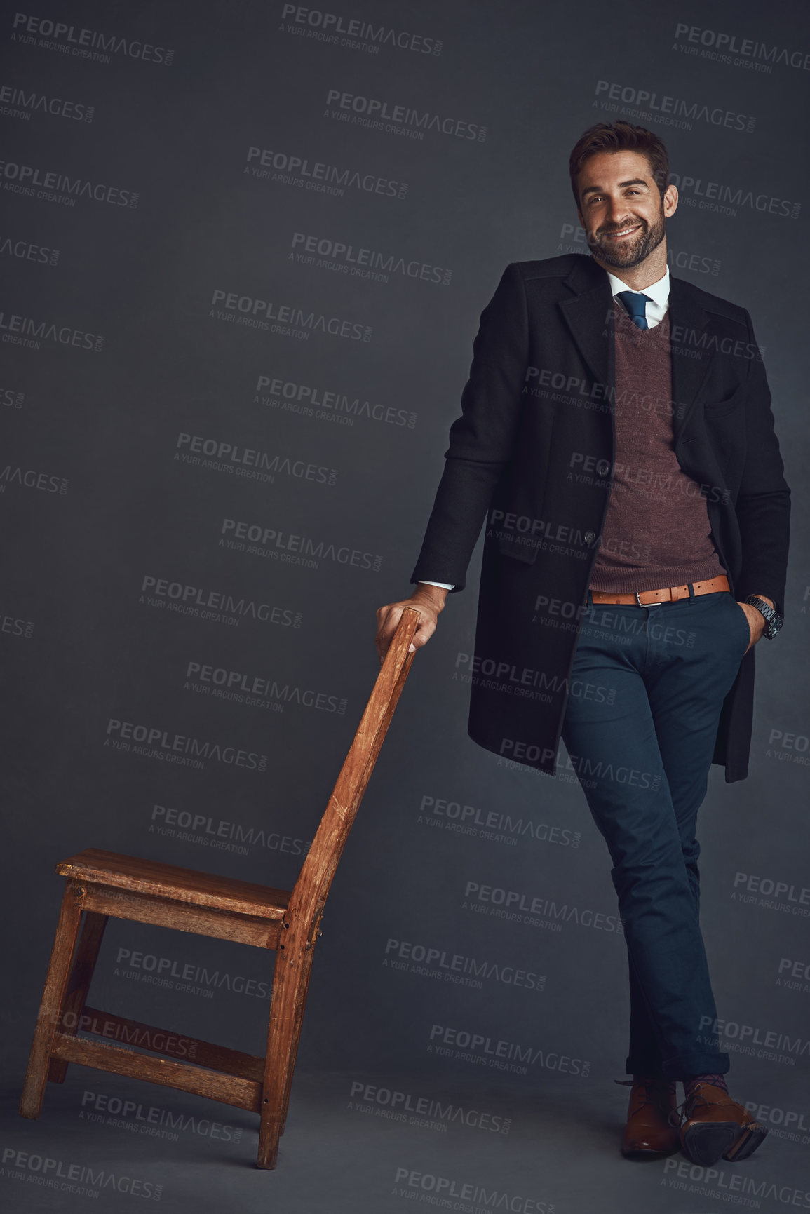 Buy stock photo Studio portrait of a stylishly dressed young man standing next to a chair against a gray background