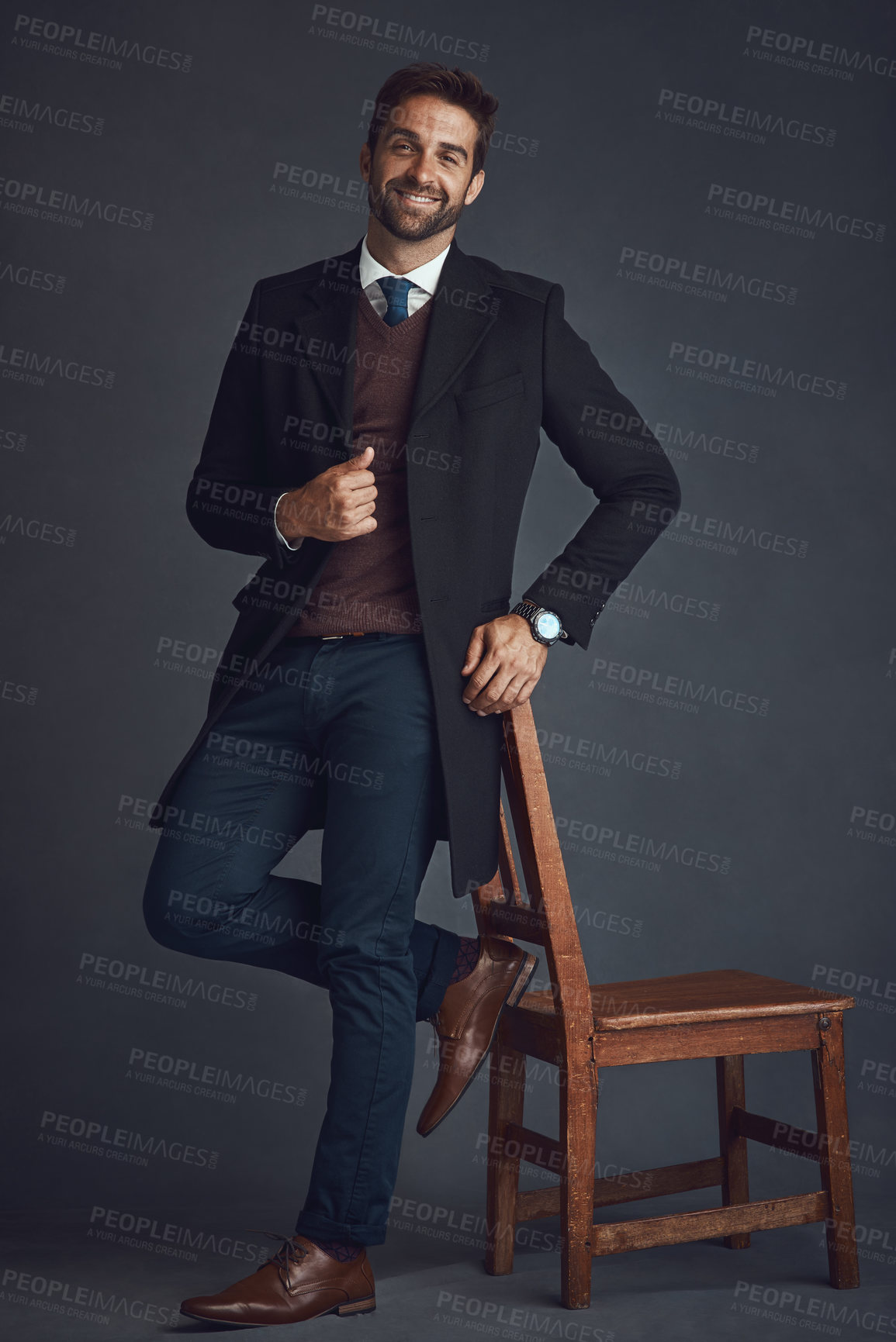 Buy stock photo Studio portrait of a stylishly dressed young man standing next to a chair against a gray background